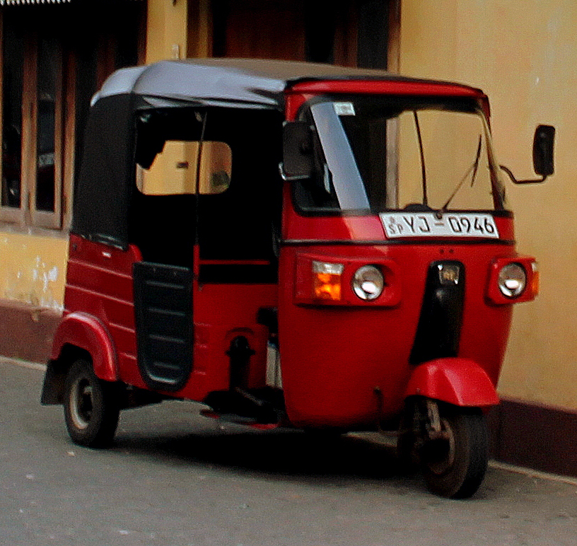 A red tuk-tuk parked on a street in Sri Lanka